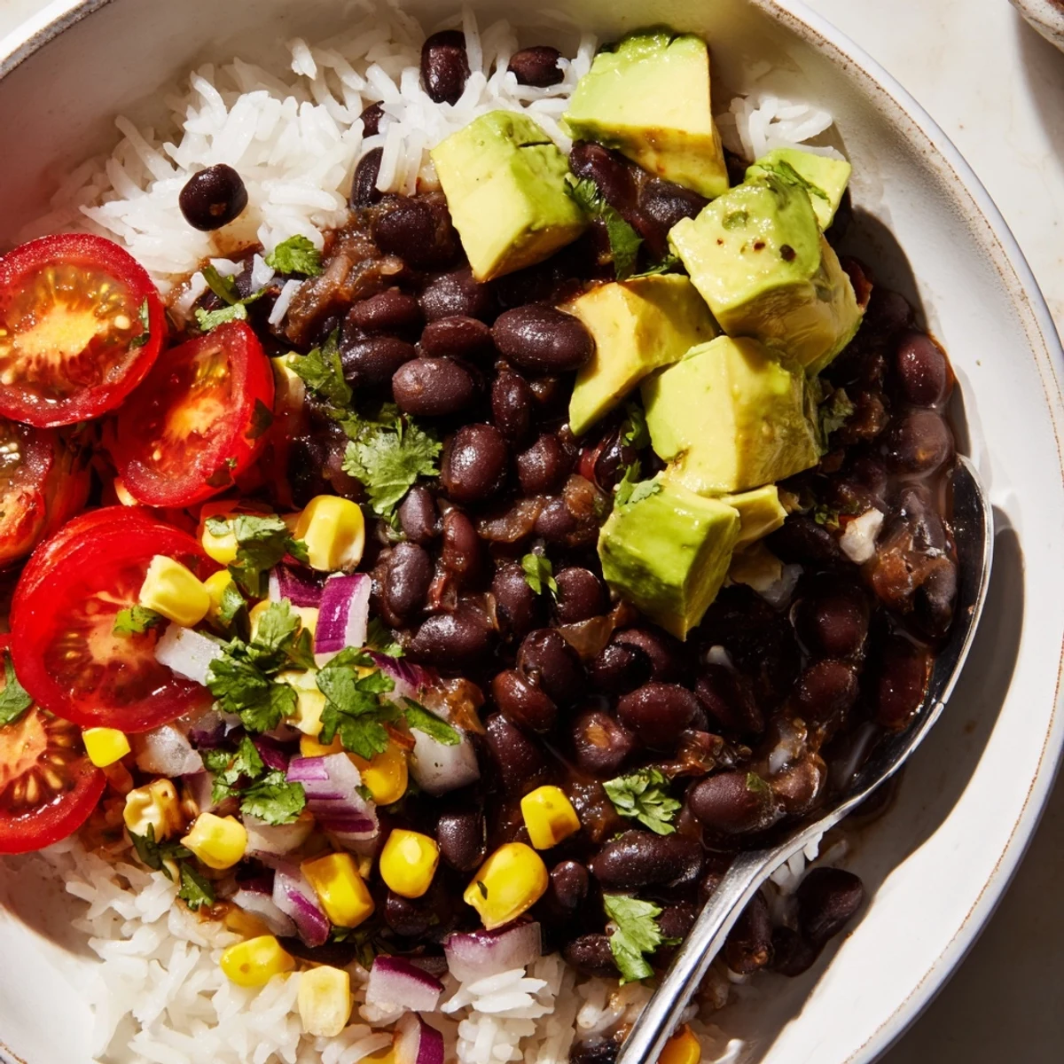 Steaming black bean and rice bowl topped with bright avocado and fresh cilantro