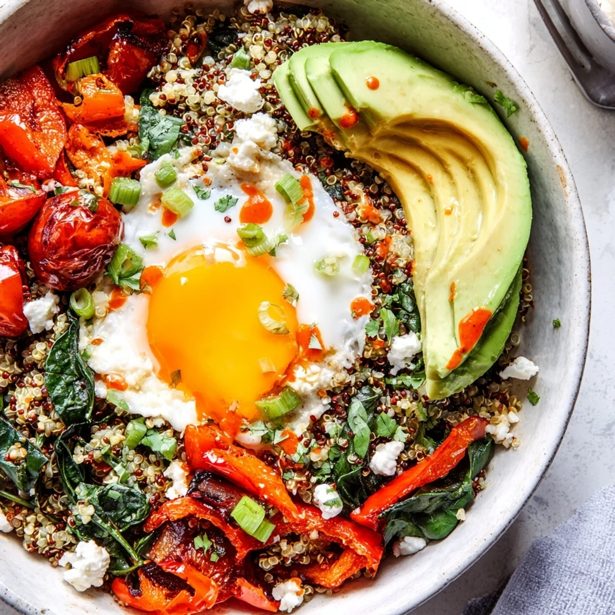 Hearty quinoa breakfast bowl with wilted spinach, roasted peppers, and a perfectly runny egg