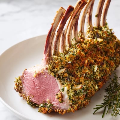 Sliced lamb chops from a roasted lamb rack reveal juicy pink interiors, served alongside roasted potatoes and green beans.