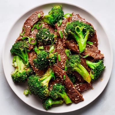 A close-up of beef and broccoli stir fry with ginger sauce, garnished with sesame seeds and green onions.