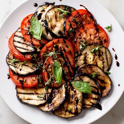 Tender charred eggplant and juicy grilled tomatoes stacked together, garnished with fragrant basil leaves