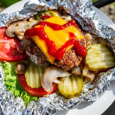 Steaming foil packets of campfire cheeseburger hobo dinner with seasoned beef and gooey cheese